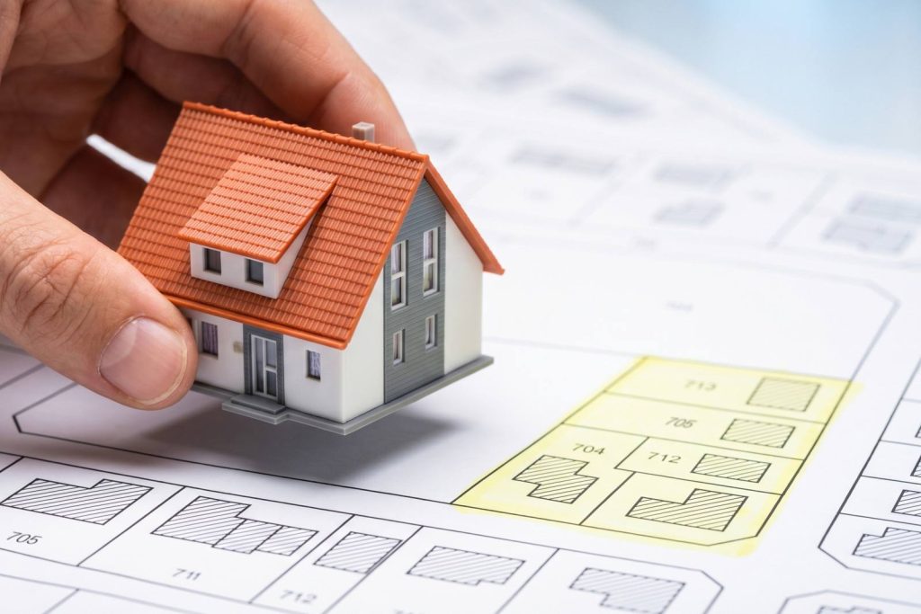 Modellhaus wird von einer Hand auf einen Bauplan gestellt